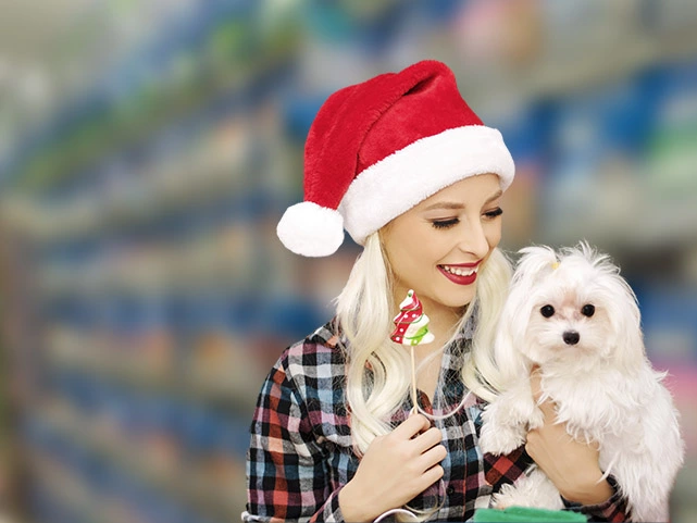 Mulher com gorro de papai noel na cabeça segurando cão