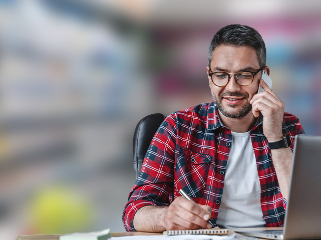 Homem falando no telefone e anotando em seu caderno