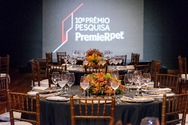 Mesas postas no salão e no fundo um telão projetando o logo do 10° Prêmio de Pesquisa PremieRpet