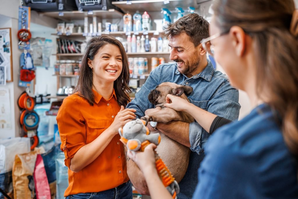Mulher sorridente abraçando homem que está segurando cão no pet shop